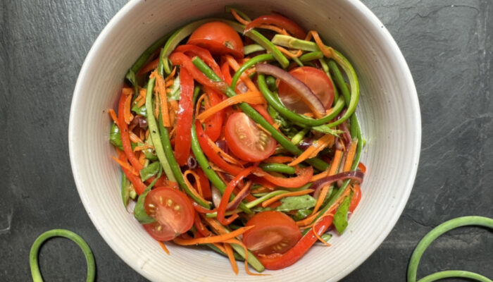 garlic scape and tomato salad in a white bowl on a black countertop