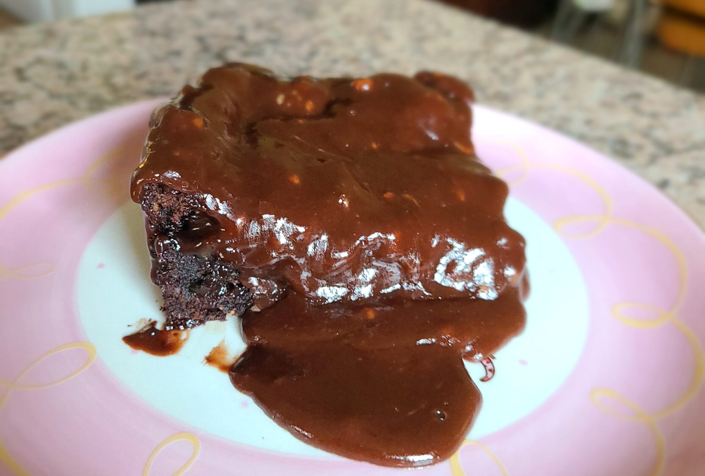 a zucchini brownie with chocolate frosting on a pink plate