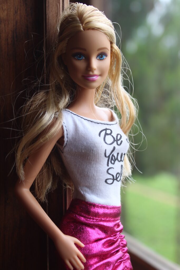 Barbie doll wearing t-shirt that says "Be Your Self" and pink skirt