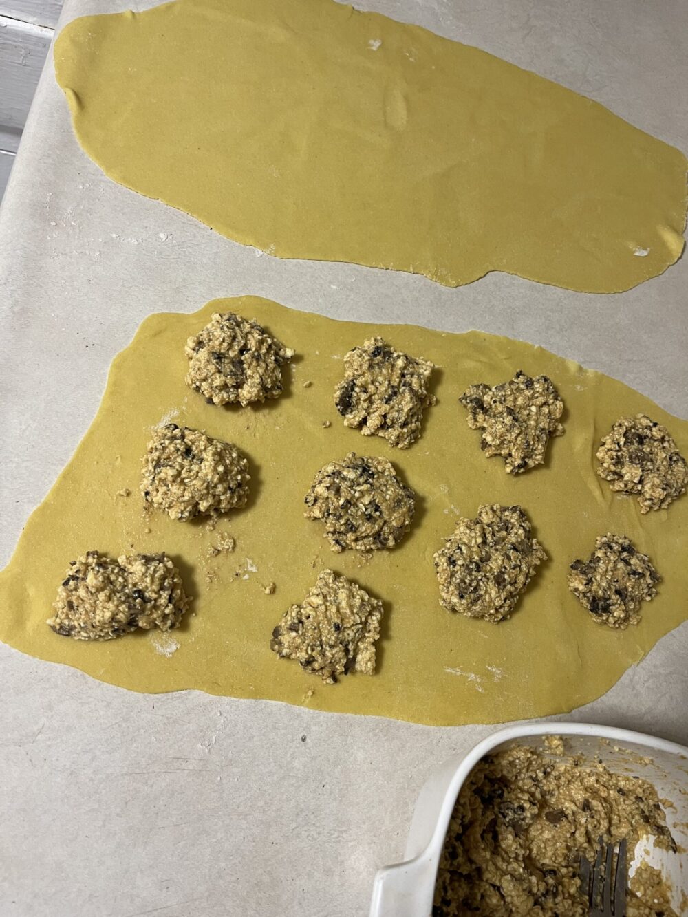 Vegan ravioli filling on a rolled out sheet of dough on a white countertop