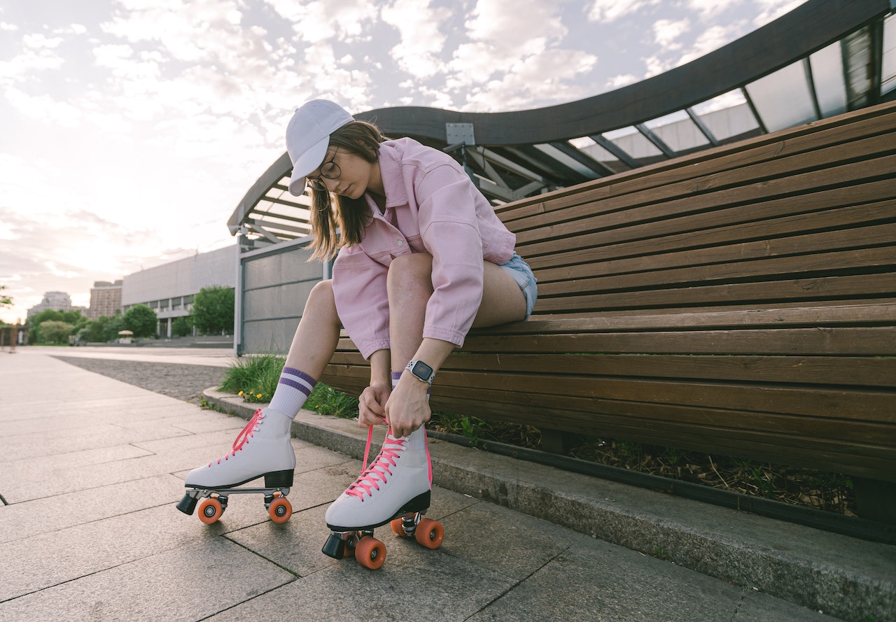 woman tying her roller blades while sitting on a wooden bench