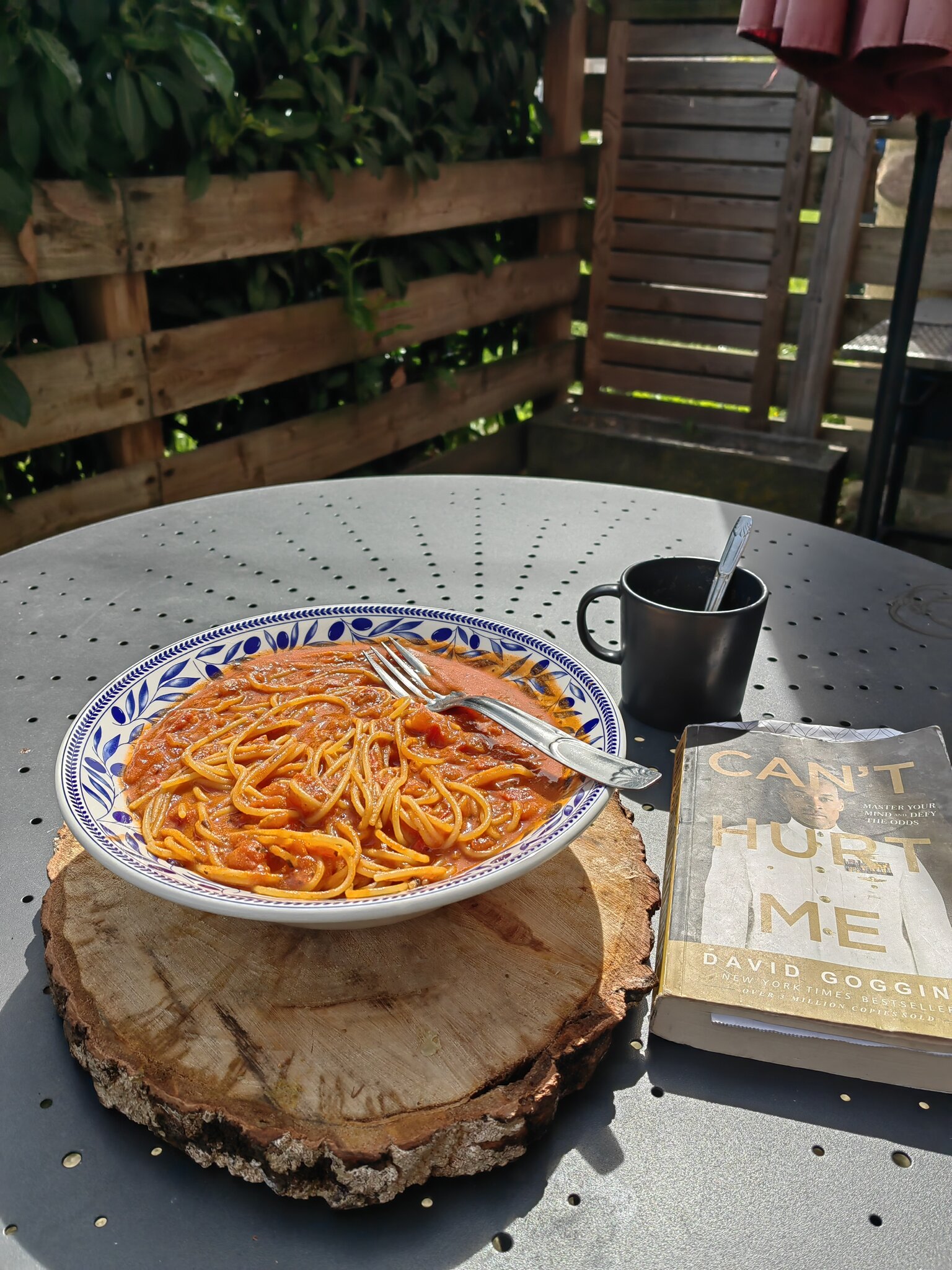 spaghetti in a bowl on a table with a mug and a book next to it