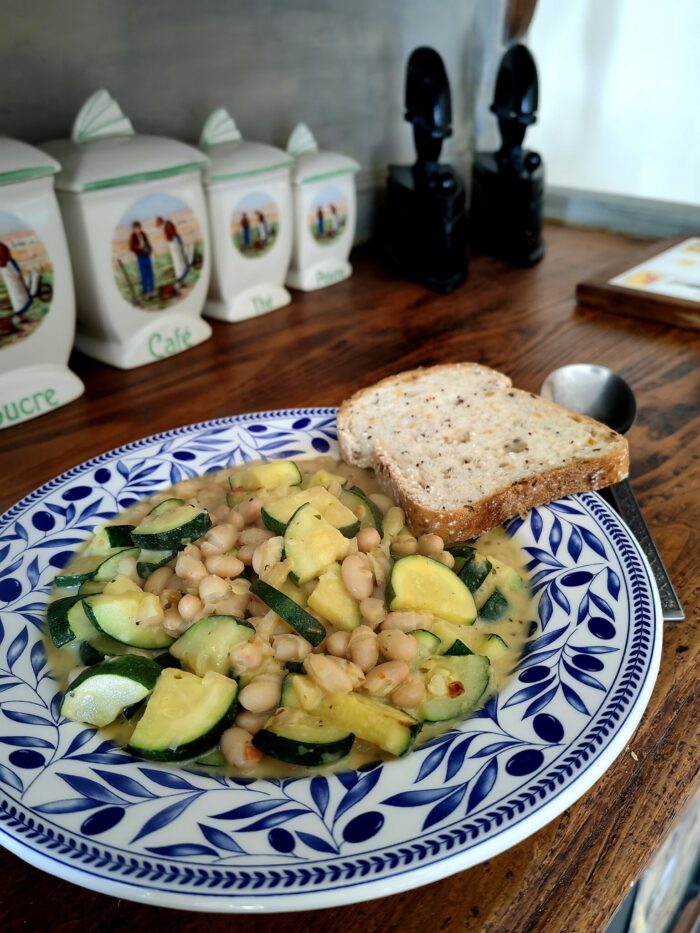 courgette in creamy garlic sauce in a blue and white floral bowl, with a side of toast, on a wooden table.