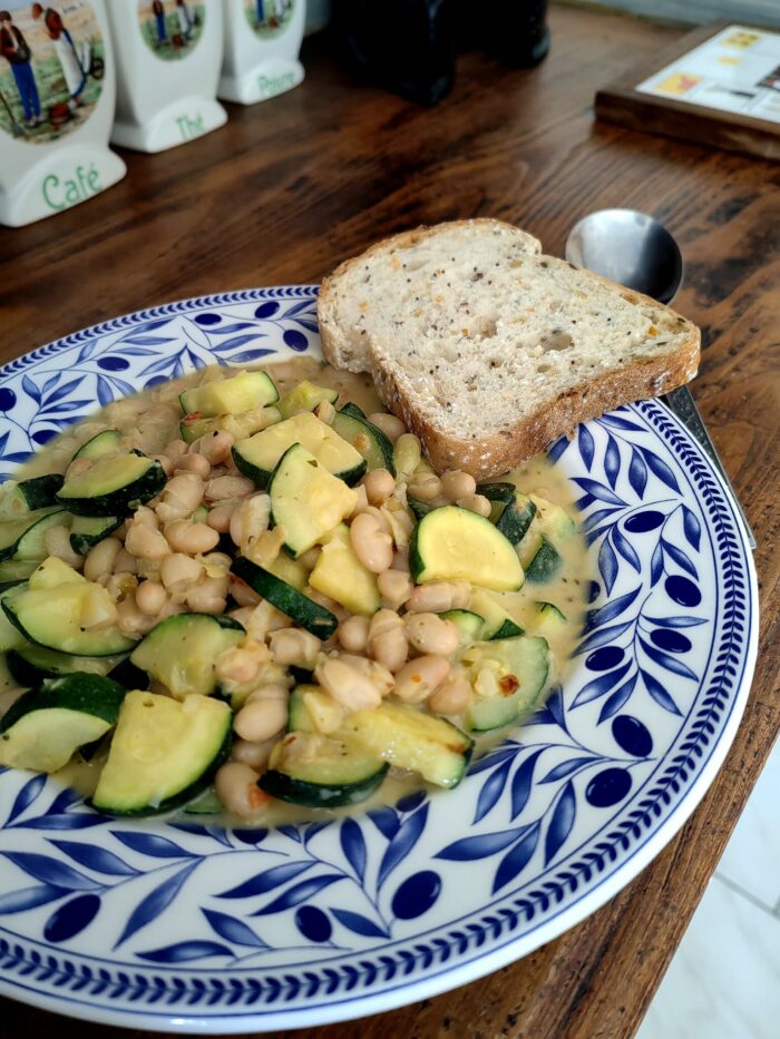 courgette in creamy garlic sauce in a blue and white floral bowl, with a side of toast, on a wooden table.