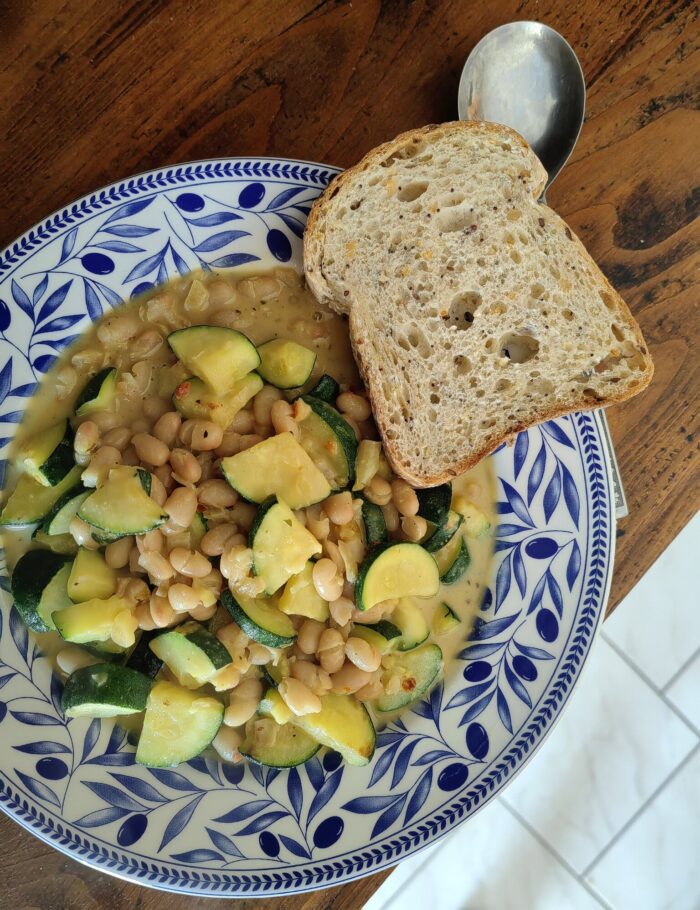 courgette in creamy garlic sauce in a blue and white floral bowl, with a side of toast, on a wooden table.